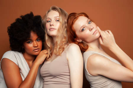 young pretty african and caucasian women posing cheerful together on brown background, lifestyle...