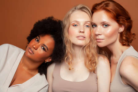 young pretty african and caucasian women posing cheerful together on brown background, lifestyle diverse nationality people conceptの写真素材