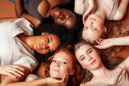 young pretty african and caucasian women posing cheerful together on brown background, lifestyle diverse nationality people conceptの写真素材