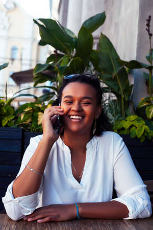 young pretty african girl posing cheerful in cafe outdoor, lifestyle people conceptの写真素材