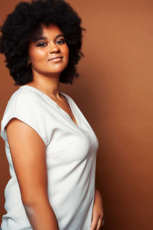 pretty young african american woman with curly hair posing cheerful gesturing on brown background, lifestyle people conceptの写真素材