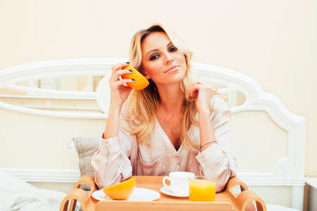 young beauty blond woman having breakfast in bed early sunny morning, princess house interior room, healthy lifestyle conceptの写真素材