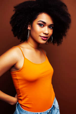 pretty young african american woman with curly hair posing cheerful gesturing on brown background, lifestyle people conceptの写真素材