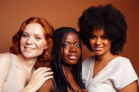 young pretty caucasian, afro, scandinavian woman posing cheerful together on brown background, lifestyle diverse nationality people conceptの写真素材