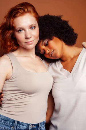 young pretty caucasian, afro woman posing cheerful together on brown background, lifestyle diverse nationality people conceptの写真素材