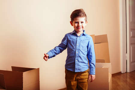 little cute boy in empty room, move to new house. home alone among boxes close up kid smiling,...