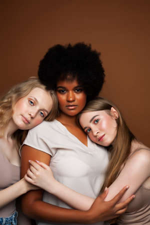 young pretty african and caucasian women posing cheerful together on brown background, lifestyle diverse nationality people conceptの写真素材