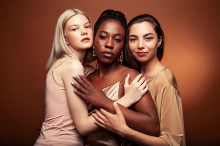 young pretty asian, caucasian, afro woman posing cheerful together on brown background, lifestyle diverse nationality people conceptの写真素材