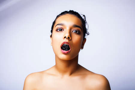 young pretty indian woman with dry fruit in mouth on white backgroundの写真素材