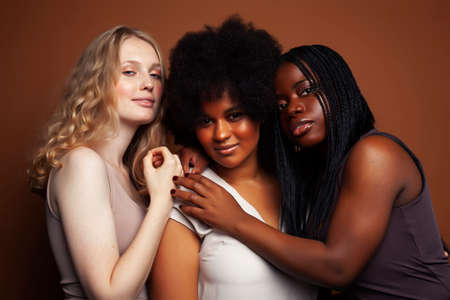 young pretty caucasian, afro, scandinavian woman posing cheerful together on brown background,...