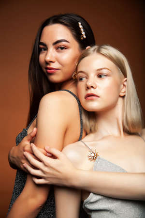 two pretty diverse girls happy posing together: blond and brunette on brown background, lifestyle people conceptの写真素材