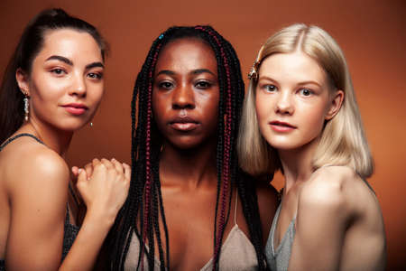 young pretty caucasian, afro, asian woman posing cheerful together on brown background, lifestyle diverse nationality people conceptの写真素材