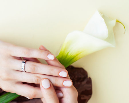 pretty perfect woman hands with white manicure and big flower on colorful yellow background, spa conceptの写真素材
