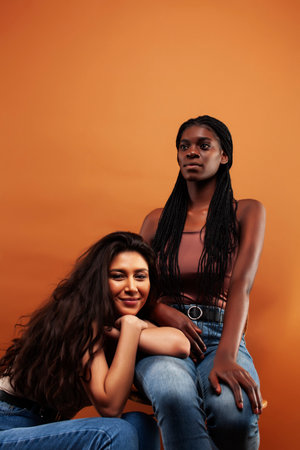young pretty asian and afro woman posing cheerful together on brown background, lifestyle diverse...