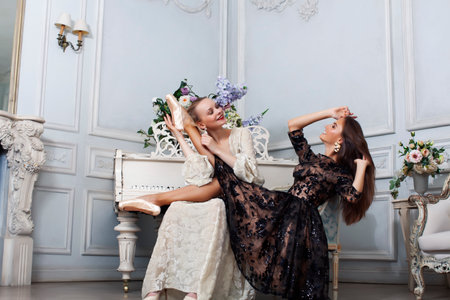 young pretty brunette ballet dancer at piano with blond woman in luxury royal interior, lifestyle...