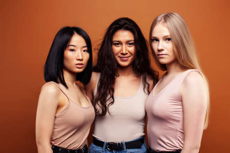 young pretty asian, caucasian, afro woman posing cheerful together on brown background, lifestyle diverse nationality people conceptの写真素材