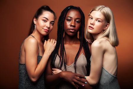 young pretty caucasian, afro, asian woman posing cheerful together on brown background, lifestyle diverse nationality people conceptの写真素材