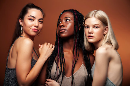 young pretty caucasian, afro, asian woman posing cheerful together on brown background, lifestyle diverse nationality people conceptの写真素材