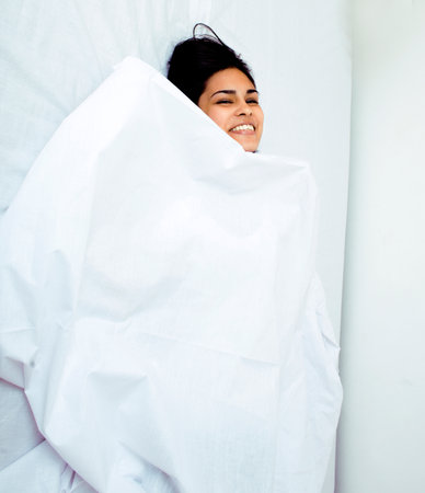 pretty indian brunette real woman in bed smiling, white sheets, tann skin close up mulatto. cant sleepの写真素材