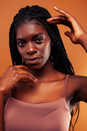 pretty young african american woman with braids posing cheerful gesturing on brown background,...
