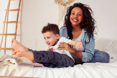 young pretty african americam mother with son in bed at morning playing, happy family, lifestyle people conceptの写真素材