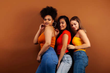 young pretty asian, caucasian, afro woman posing cheerful together on brown background, lifestyle diverse nationality people conceptの写真素材
