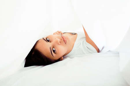 young pretty tann woman in bed among white sheets having fun, trying to sleep, fooling around