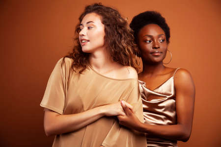 two pretty girls african and caucasian blond posing cheerful together on brown background, ethnicity diverse lifestyle people conceptの写真素材