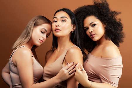 young pretty asian, caucasian, afro woman posing cheerful together on brown background, lifestyle diverse nationality people conceptの写真素材