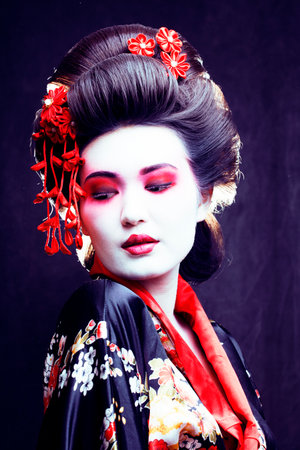 young pretty real geisha in kimono with sakura and decoration on black backgroundの写真素材