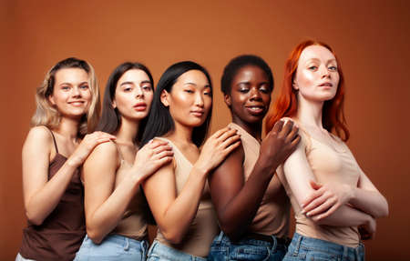 young pretty caucasian, afro, asian, scandinavian woman posing cheerful together on brown background, lifestyle diverse nationality people conceptの写真素材