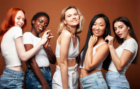 young pretty caucasian, afro, asian, scandinavian woman posing cheerful together on brown background, lifestyle diverse nationality people conceptの写真素材