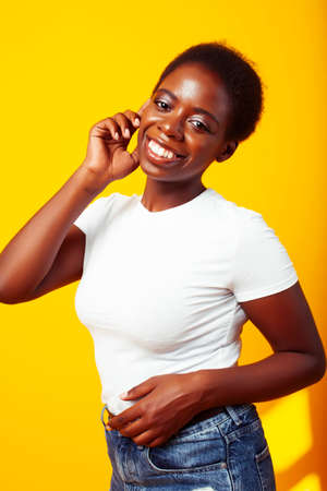 pretty young african american woman with curly hair posing cheerful gesturing on yellow background,...