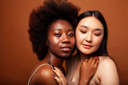 young pretty asian, afro woman posing cheerful together on brown background, lifestyle diverse nationality people conceptの写真素材