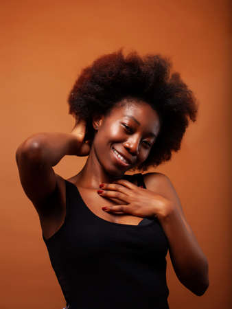pretty young african american woman with curly hair posing cheerful gesturing on brown background,...