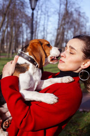 pretty young girl in red coat playing with dog outside in green park, lifestyle people conceptの写真素材