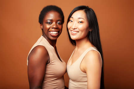 young pretty asian, afro woman posing cheerful together on brown background, lifestyle diverse...