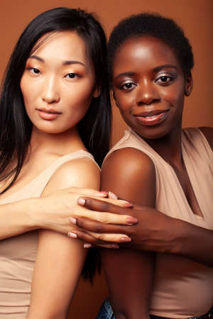 young pretty asian, afro woman posing cheerful together on brown background, lifestyle diverse nationality people conceptの写真素材