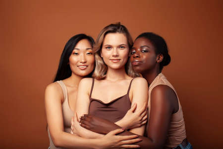 young pretty caucasian, afro, scandinavian woman posing cheerful together on brown background, lifestyle diverse nationality people conceptの写真素材