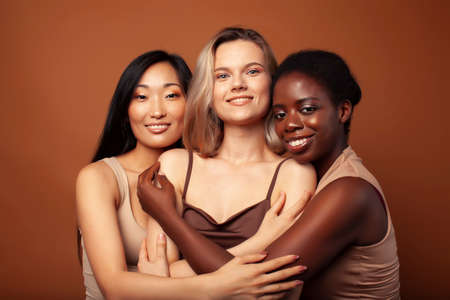 young pretty caucasian, afro, scandinavian woman posing cheerful together on brown background, lifestyle diverse nationality people conceptの写真素材