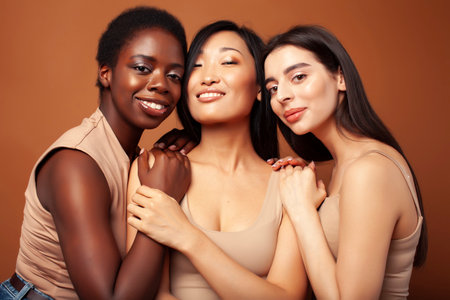 young pretty caucasian, afro, scandinavian woman posing cheerful together on brown background, lifestyle diverse nationality people conceptの写真素材