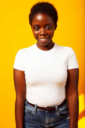 pretty young african american woman with curly hair posing cheerful gesturing on yellow background,...