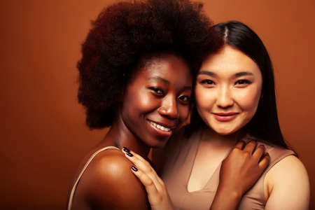 young pretty asian, afro woman posing cheerful together on brown background, lifestyle diverse nationality people conceptの写真素材