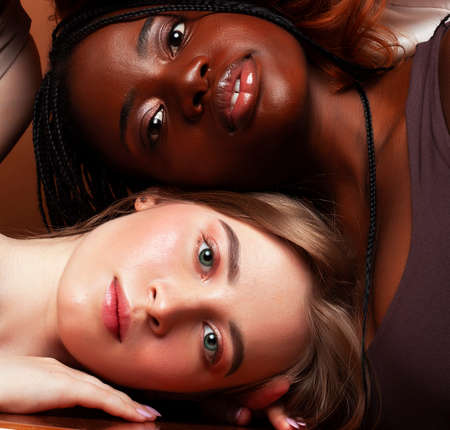 young pretty african and caucasian women posing cheerful together on brown background, lifestyle diverse nationality people conceptの写真素材