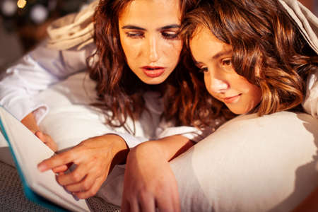 young pretty girls in bed at Christmass morning, happy family smiling lifestyle at holiday reading bookの写真素材