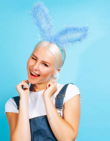 young pretty blond girl with rabbit ears posing cheerful on blue background, lifestyle people...