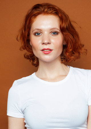 young pretty redhead girl posing cheerful on warm brown background, lifestyle people concept