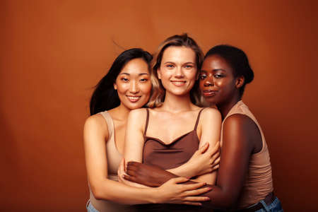 young pretty african and caucasian women posing cheerful together on brown background, lifestyle diverse nationality people conceptの写真素材
