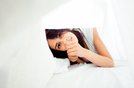 young pretty tann woman in bed among white sheets having fun, trying to sleep, fooling aroundの写真素材