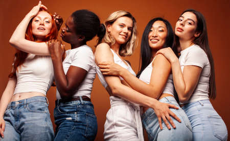 young pretty african and caucasian women posing cheerful together on brown background, lifestyle diverse nationality people conceptの写真素材